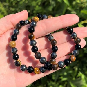 Pode incluir: Um bracelete feito com contas pretas, marrons e prateadas. O bracelete &eacute; feito com contas de olho de tigre, hematita e &ocirc;nix.