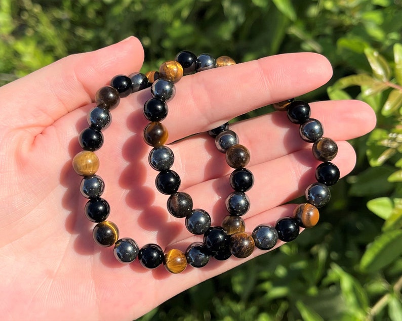 Pode incluir: Um bracelete feito com contas pretas, marrons e prateadas. O bracelete &eacute; feito com contas de olho de tigre, hematita e &ocirc;nix.