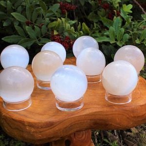 Op de afbeelding: Een verzameling van tien witte seleniet bollen gepresenteerd op een houten standaard. De bollen zijn glad en gepolijst, met een subtiele iriserende glans.