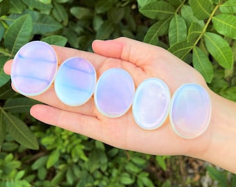 May include: Six iridescent opalite palm stones in various shades of white, pink, and blue. The stones are smooth and polished, and they are arranged in a row on a hand.