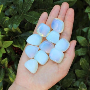 May include: A collection of white opal tumbled stones with iridescent rainbow flashes. The stones are smooth and polished, and they are arranged in a hand.