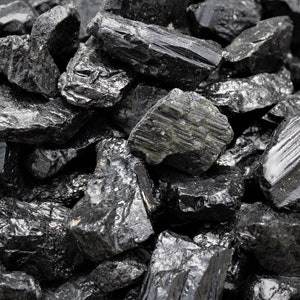 May include: A close-up of a pile of black obsidian stones. The stones are rough and have a shiny, almost glassy surface.