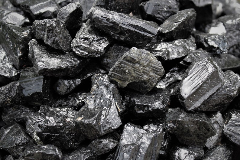 May include: A close-up of a pile of black obsidian stones. The stones are rough and have a shiny, almost glassy surface.