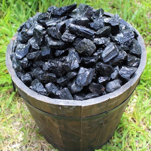 May include: A wooden bucket filled with black tourmaline crystals. The crystals are rough and have a natural, unpolished look.