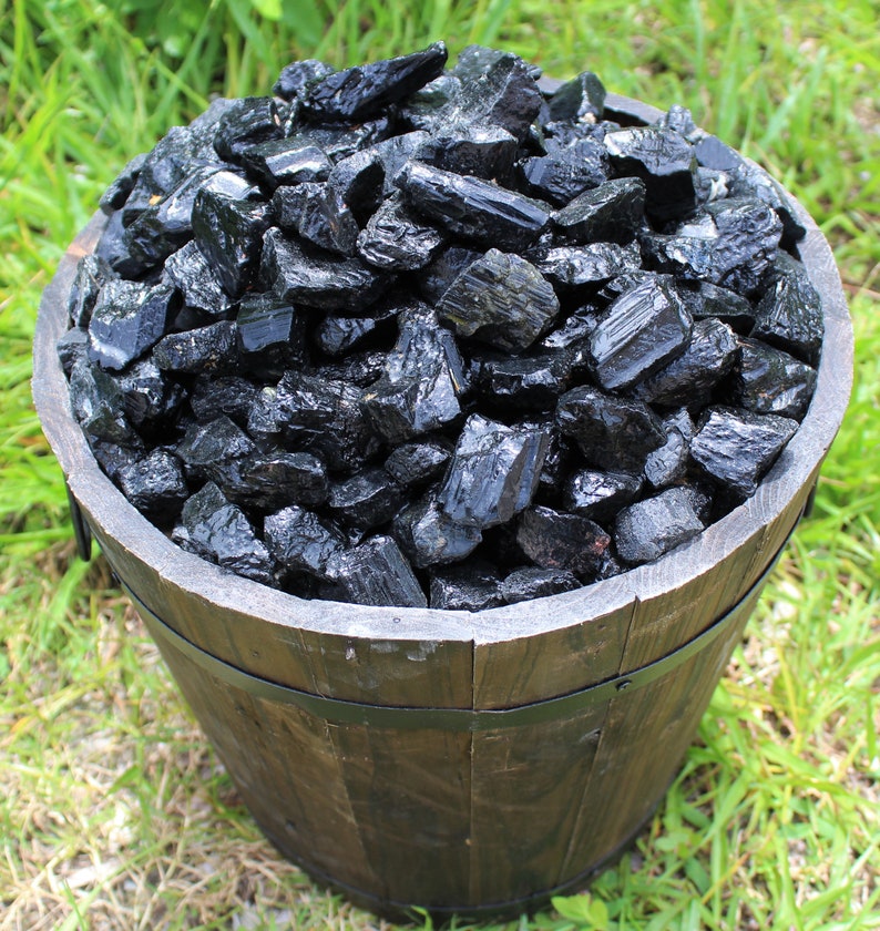 May include: A wooden bucket filled with black tourmaline crystals. The crystals are rough and have a natural, unpolished look.