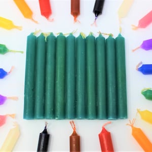 May include: A group of 15 green pillar candles arranged in a rectangle on a white surface. The candles are surrounded by a variety of colored candles, including red, orange, yellow, green, blue, purple, and brown.