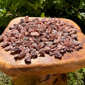 May include: A collection of small, irregular copper nuggets with a metallic, reddish-brown finish and dark, textured inclusions. The pieces vary in shape and size, displaying a raw, unrefined appearance with a bright, reflective surface quality.