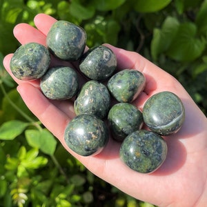 May include: A collection of green aventurine tumbled stones. The stones are smooth and polished, with a variety of shades of green. They are arranged in a hand, with the palm facing up.