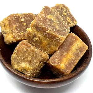 May include: A wooden bowl filled with several pieces of brown, rectangular, and irregularly shaped blocks. The blocks have a rough, granular texture and a light brown, almost golden hue. The bowl is dark brown.