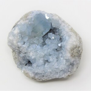 May include: A light blue celestite crystal cluster in a natural rock formation. The crystal is clear and has a glassy luster. The rock is gray and has a rough texture.