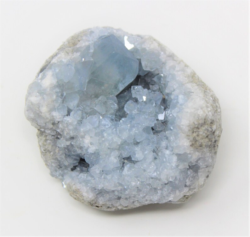 May include: A light blue celestite crystal cluster in a natural rock formation. The crystal is clear and has a glassy luster. The rock is gray and has a rough texture.