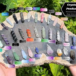 May include: A variety of crystal pendants wrapped in silver wire. The pendants are arranged in a circle on a wooden surface. The crystals include amethyst, rose quartz, clear quartz, sodalite, and more.