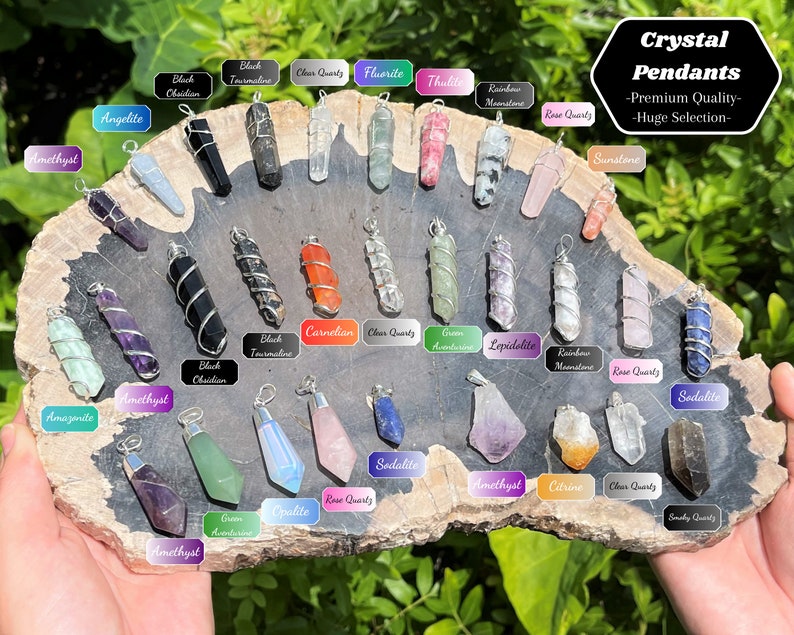 May include: A variety of crystal pendants wrapped in silver wire. The pendants are arranged in a circle on a wooden surface. The crystals include amethyst, rose quartz, clear quartz, sodalite, and more.