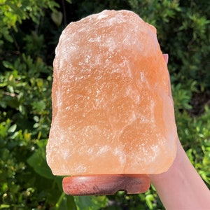 May include: A large, natural Himalayan salt lamp with a warm, orange-pink hue. The lamp is sitting on a wooden base.