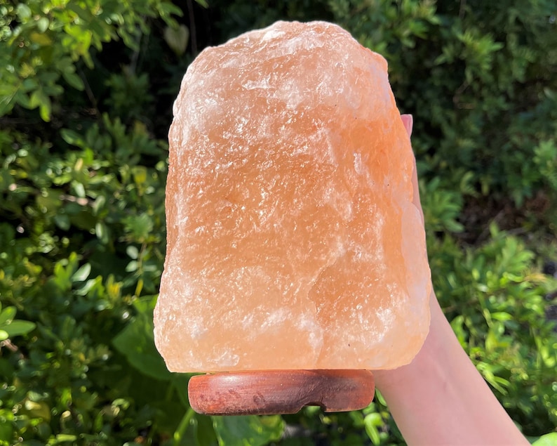 May include: A large, natural Himalayan salt lamp with a warm, orange-pink hue. The lamp is sitting on a wooden base.