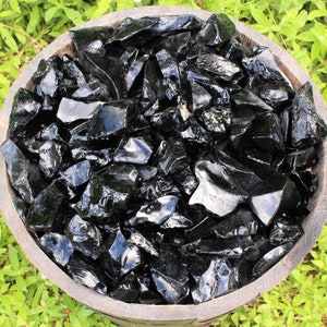 Puede incluir: Un cuenco de madera lleno de trozos de obsidiana negra. El cuenco est&aacute; sentado sobre un lecho de hierba verde.