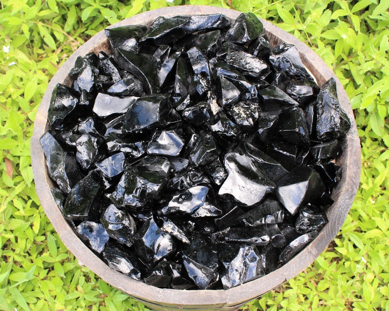Puede incluir: Un cuenco de madera lleno de trozos de obsidiana negra. El cuenco est&aacute; sentado sobre un lecho de hierba verde.