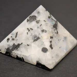 Puede incluir: Un objeto decorativo en forma de pir&aacute;mide hecho de piedra moteada blanca y negra. La pir&aacute;mide tiene una base plana y cuatro lados triangulares que se unen en un punto. La piedra tiene una superficie pulida y lisa.