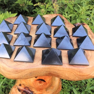 May include: A collection of 16 black obsidian pyramids arranged in a grid pattern on a wooden surface. The pyramids are all the same size and shape, and they are polished to a smooth finish.