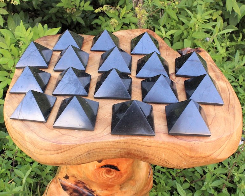May include: A collection of 16 black obsidian pyramids arranged in a grid pattern on a wooden surface. The pyramids are all the same size and shape, and they are polished to a smooth finish.