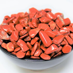 Puede incluir: Un cuenco lleno de piedras de jaspe rojo pulidas. Las piedras son lisas y pulidas, de un color rojo intenso.