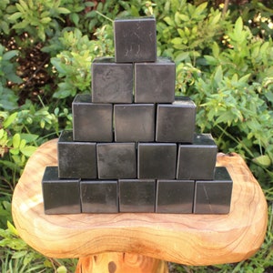 May include: A pyramid of 15 black obsidian cubes stacked on a wooden surface. The cubes are smooth and polished.