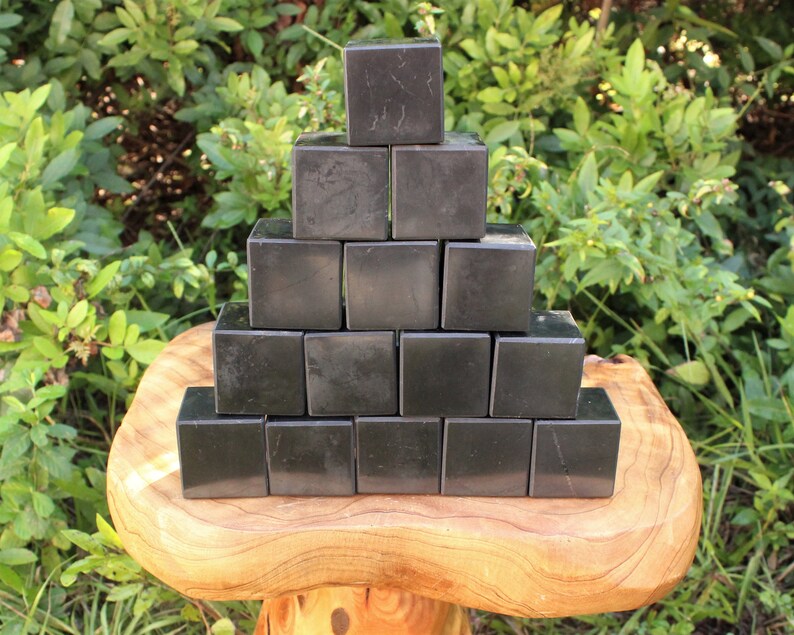 May include: A pyramid of 15 black obsidian cubes stacked on a wooden surface. The cubes are smooth and polished.