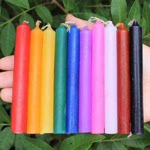 May include: A set of 10 small, thin, colored candles. The candles are arranged in a rainbow order, from red to black. The candles are about 6 inches long.