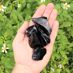 Puede incluir: Una mano sosteniendo una colecci&oacute;n de piedras de obsidiana negra. Las piedras son &aacute;speras y tienen un brillo vidrioso.