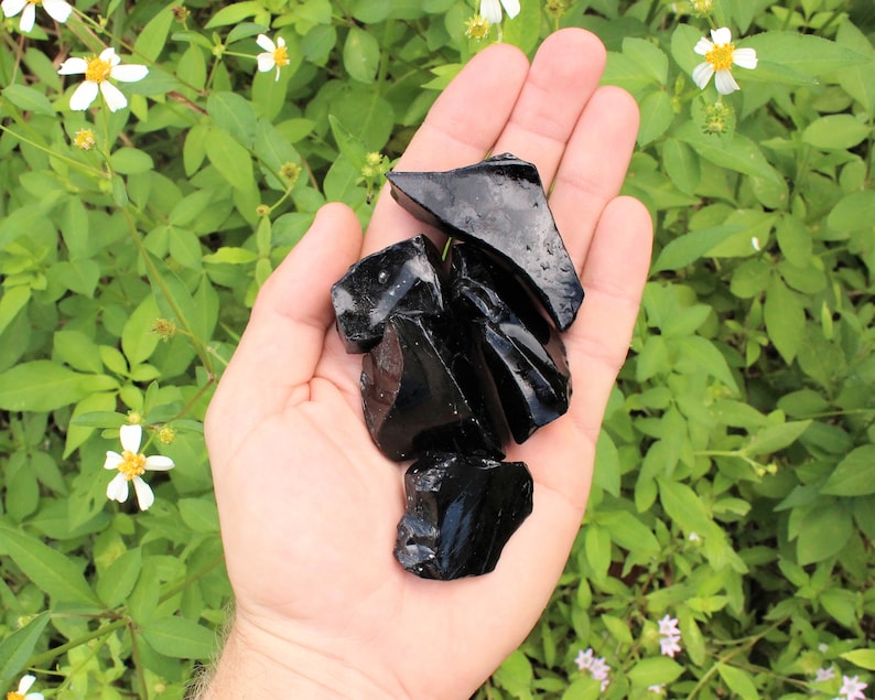 Puede incluir: Una mano sosteniendo una colecci&oacute;n de piedras de obsidiana negra. Las piedras son &aacute;speras y tienen un brillo vidrioso.
