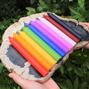 May include: A set of ten colorful candles arranged in a rainbow pattern on a piece of petrified wood. The candles are all the same size and shape, and they are arranged in order from red to violet.