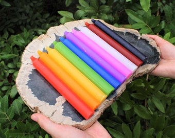 May include: A set of ten colorful candles arranged in a rainbow pattern on a piece of petrified wood. The candles are all the same size and shape, and they are arranged in order from red to violet.