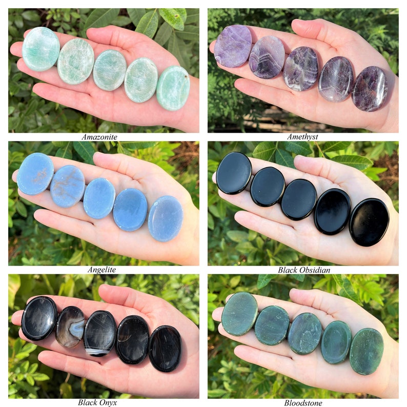 May include: An assortment of smooth, polished palm stones in various colours, including green, purple, blue, black, and grey. The stones are arranged in rows of four, with each row representing a different type of stone. The stones are held in a hand, with the fingers spread out to show the size and shape of the stones.