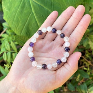 May include: A bracelet made of white and purple beads. The bracelet is made of clear quartz and amethyst beads.