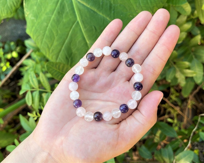 May include: A bracelet made of white and purple beads. The bracelet is made of clear quartz and amethyst beads.