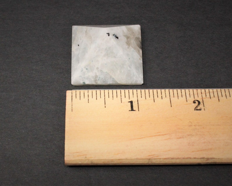 Puede incluir: Una pir&aacute;mide cuadrada de piedra de color claro con una regla al lado. La pir&aacute;mide tiene un aspecto veteado blanco y gris con peque&ntilde;as motas negras. La regla es de madera y muestra medidas en cent&iacute;metros.
