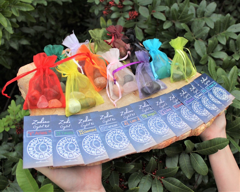 K&ouml;nnte beinhalten: Zw&ouml;lf kleine Beutel mit Kristallen, jeder in einer anderen Farbe und einer Karte mit einem Sternzeichen und den Worten "Zodiac Crystal Kit".