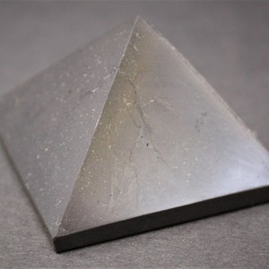 May include: A black obsidian pyramid crystal with a smooth, polished surface. The crystal has a slight sheen and is slightly translucent.