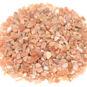 May include: A large pile of small, smooth, peach-colored sunstone chips. The chips are various shapes and sizes, with a slight shimmer.