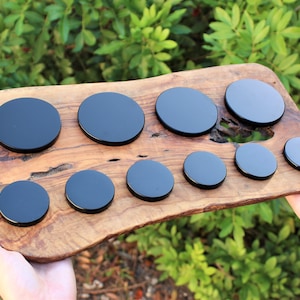 May include: A set of ten black round coasters of varying sizes on a wooden surface.