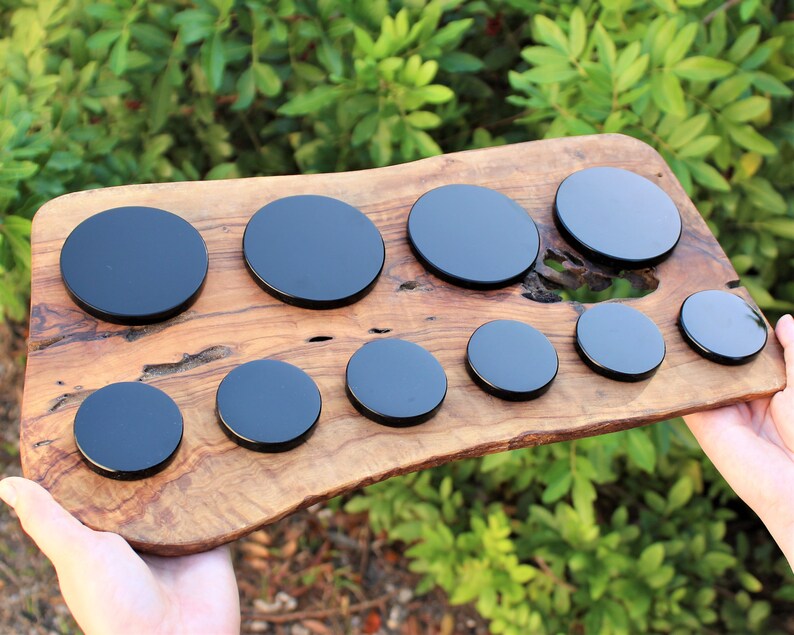 May include: A set of ten black round coasters of varying sizes on a wooden surface.