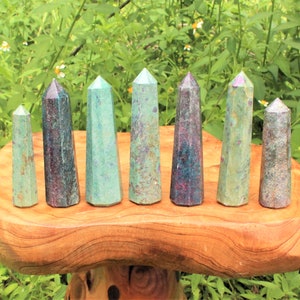May include: A set of eight green and purple gemstone points, also known as ruby in zoisite, arranged on a wooden surface. The points are various sizes and shapes.
