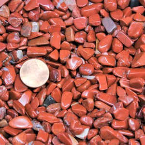 Puede incluir: Primer plano de un mont&oacute;n de piedras de jaspe rojo pulidas. Las piedras son de varios tama&ntilde;os y formas, y todas son lisas y pulidas. Se incluye una moneda de un centavo de d&oacute;lar estadounidense para la escala.