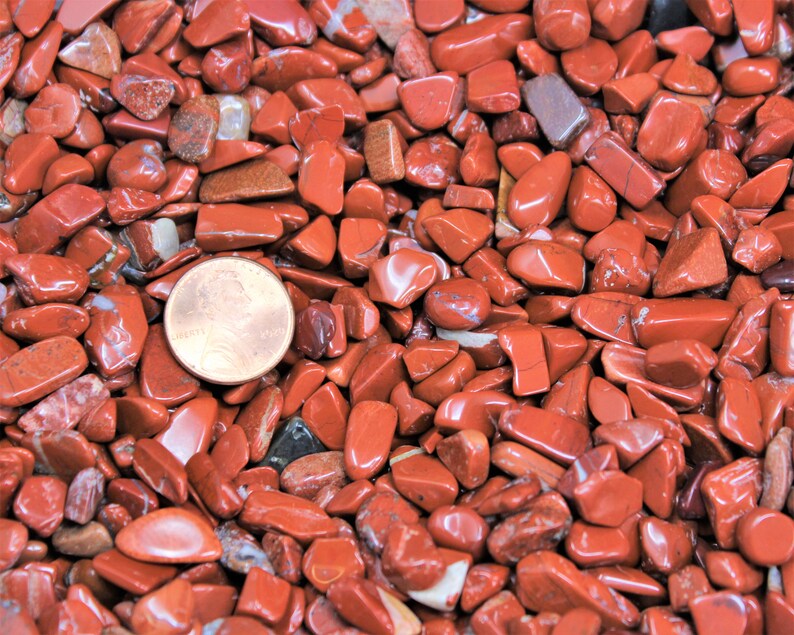 Puede incluir: Primer plano de un mont&oacute;n de piedras de jaspe rojo pulidas. Las piedras son de varios tama&ntilde;os y formas, y todas son lisas y pulidas. Se incluye una moneda de un centavo de d&oacute;lar estadounidense para la escala.