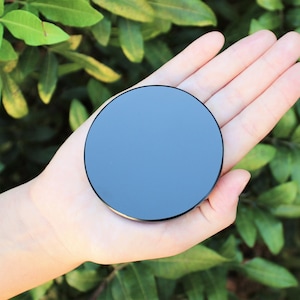 May include: A black round object with a smooth, reflective surface. The object is being held in a person's hand.