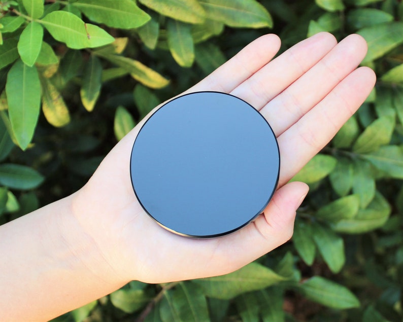 May include: A black round object with a smooth, reflective surface. The object is being held in a person's hand.