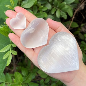 Selenite Hearts in three sizes in the palm of a hand.