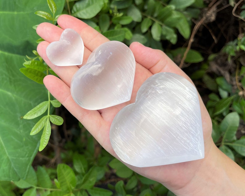 Selenite Hearts in three sizes in the palm of a hand.