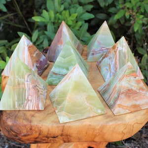 May include: Nine green, brown, and white onyx pyramids arranged on a wooden surface. The pyramids are all different sizes and shapes.
