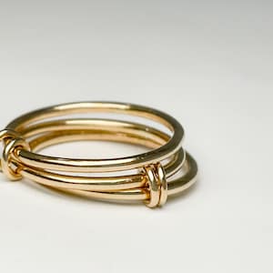 May include: A gold ring with three bands intertwined. The bands are smooth and polished.